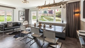 A modern kitchen with a dining area, large windows, and a view of the garden. - Haus Granit Zermatt (Zermatt)