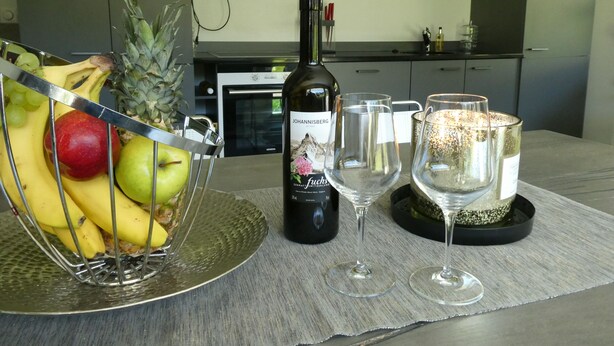 A kitchen with a fruit basket, a wine bottle, and two wine glasses on a table. - Haus Granit Zermatt (Zermatt)