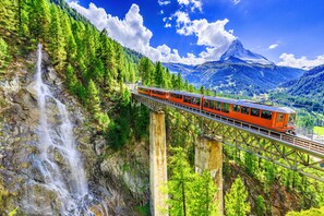 A train on a bridge over a waterfall in a mountainous area. - Haus Venus (Zermatt)