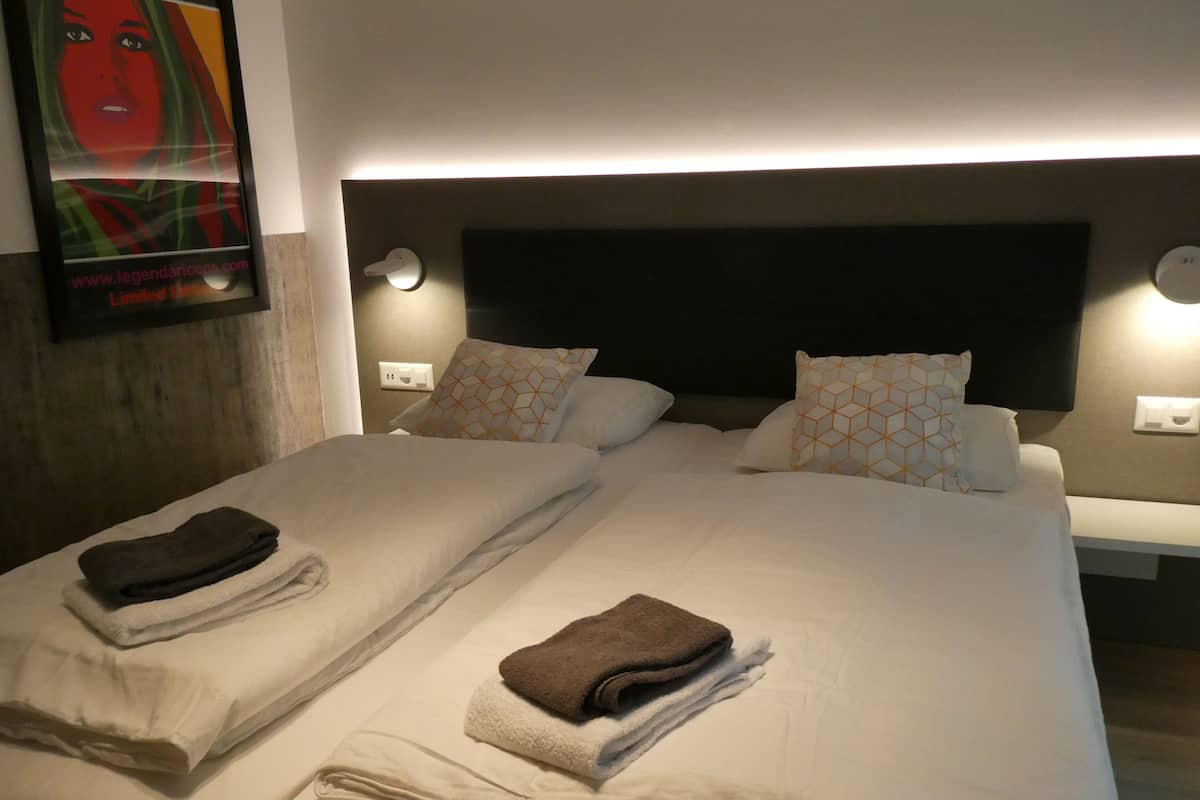 A hotel room with two beds, each with neatly folded towels and patterned pillows.