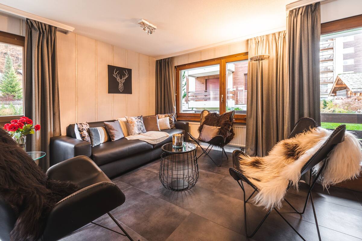 A modern living room with a sofa, chairs, a coffee table, and a view of the outdoors.