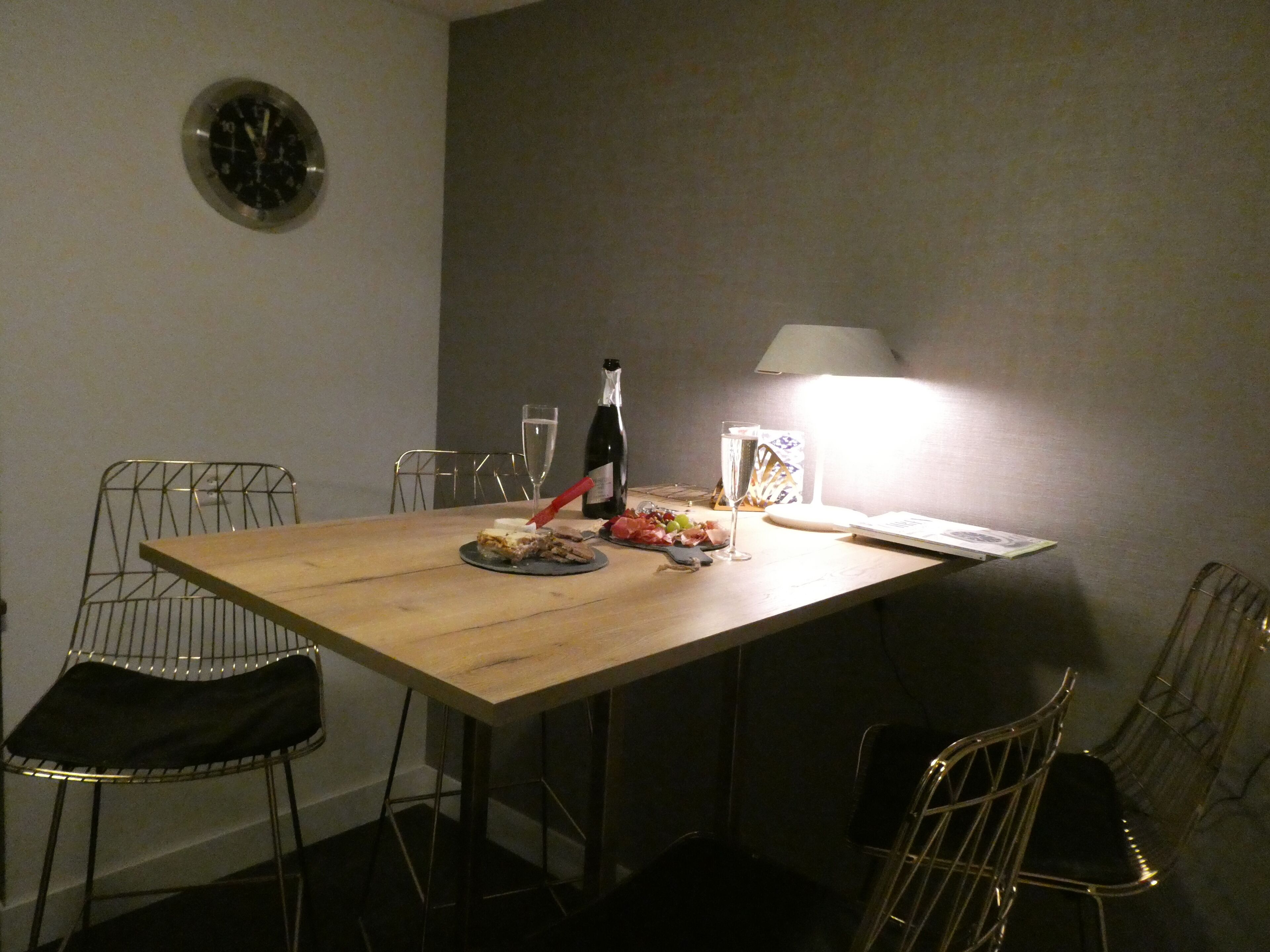 Ett matbord med stolar, en flaska vin, ett glas vatten och en lampa.