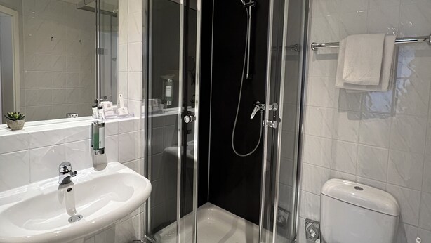 A modern bathroom with a glass-enclosed shower, a white sink, and a toilet. - Hotel am Mühlenteich (Schwelm)