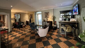 Een ruime woonkamer met een zwart-wit betegelde vloer, een bar met televisie, en een zithoek met een bank en fauteuils.