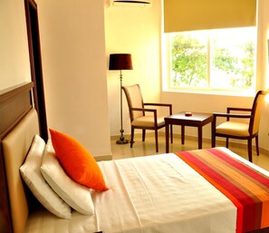 A hotel room with a bed, two chairs, a small table, and a lamp. - Sai Sea City Hotel (Colombo)