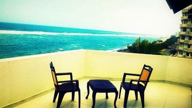 A balcony with two chairs and a small table, overlooking a beach with the ocean. - Sai Sea City Hotel (Colombo)