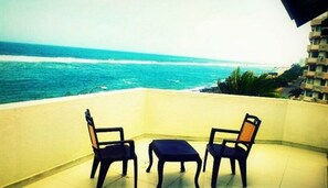 A balcony with two chairs and a small table, overlooking a beach with the ocean. - Sai Sea City Hotel (Colombo)