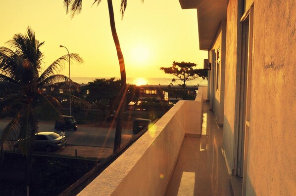 A balcony overlooking a street with a sunset, palm trees, and a building with a balcony. - Sai Sea City Hotel (Colombo)