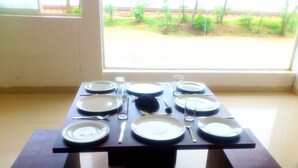 A dining table set with plates, cutlery, and glasses, positioned near a window with a view of greenery. - Sai Sea City Hotel (Colombo)