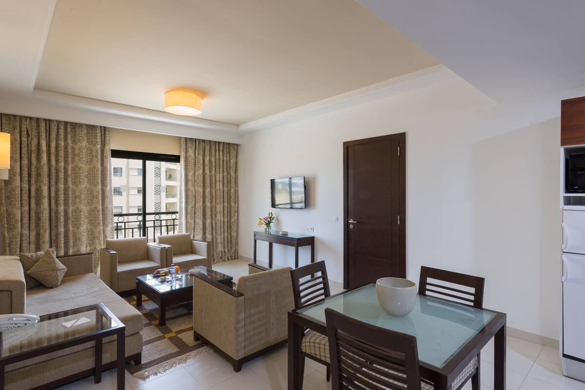 A hotel room with a living area, a dining table, a sofa, a coffee table, and a TV mounted on the wall.