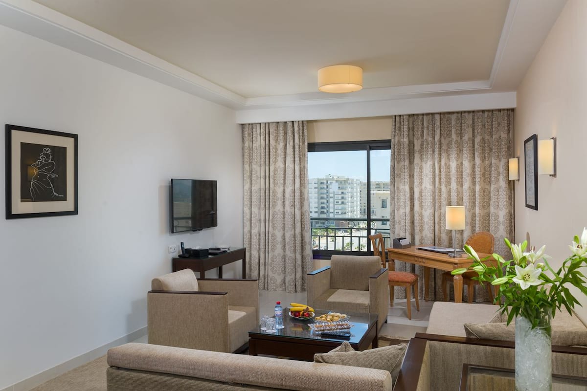 A hotel room with a balcony, a TV, a dining table, and a sofa.