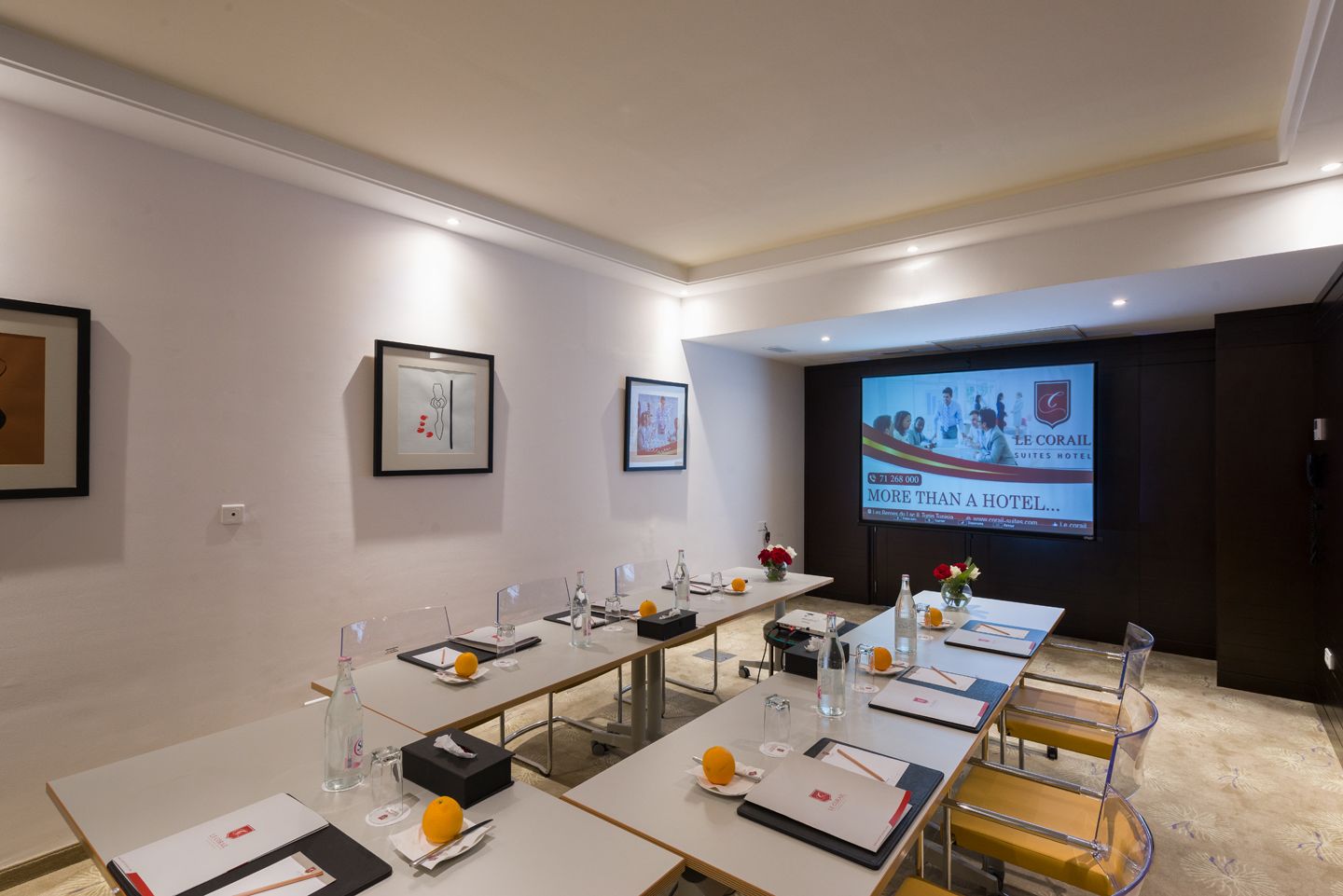 A conference room with long tables, chairs, and a projection screen displaying hotel information.