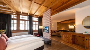 A hotel room with a wooden ceiling, a bed with white linens, a red chair, a sofa, a wooden cabinet, and a large mirror. - Hotel Parsenn (Davos)