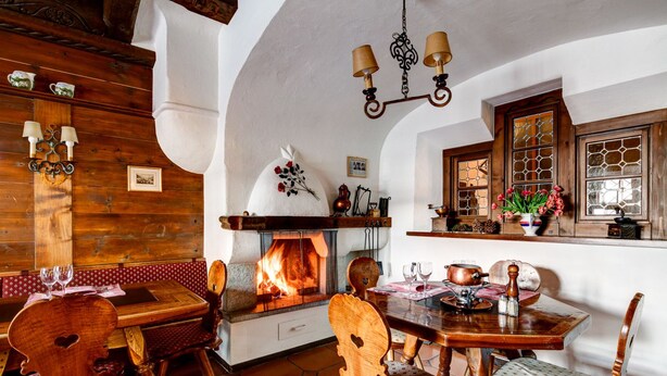 A rustic dining room with a fireplace, wooden furniture, and a tiled floor. - Hotel Parsenn (Davos)