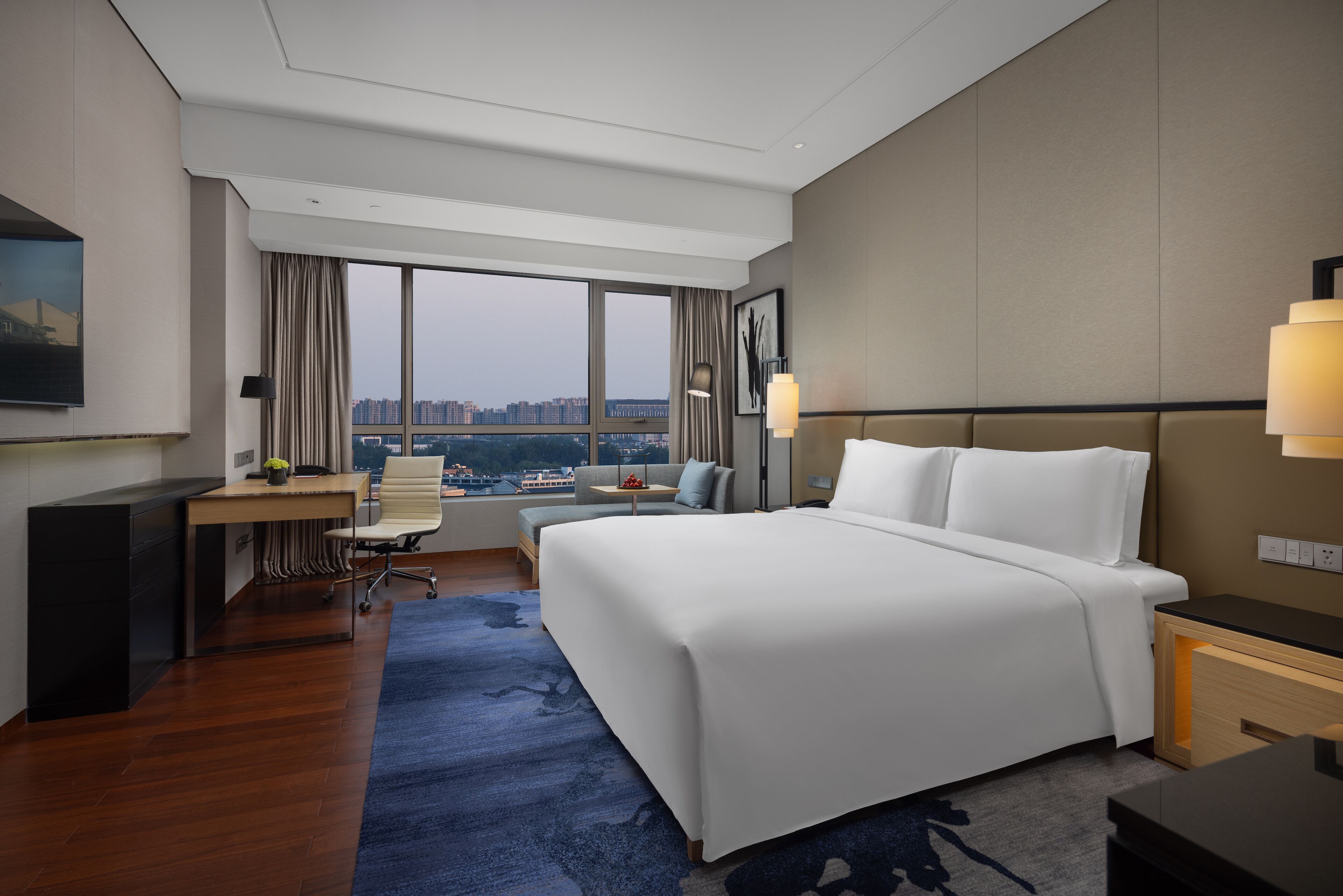 A hotel room with a large bed, a desk with a chair, a small table, and a TV on the wall.