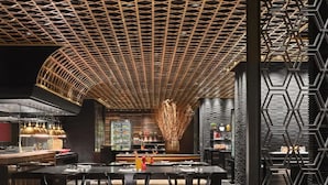 Un restaurant moderne avec un intérieur élégant, un plafond à motifs géométriques originaux, un bar central et un aménagement des places assises soigné.