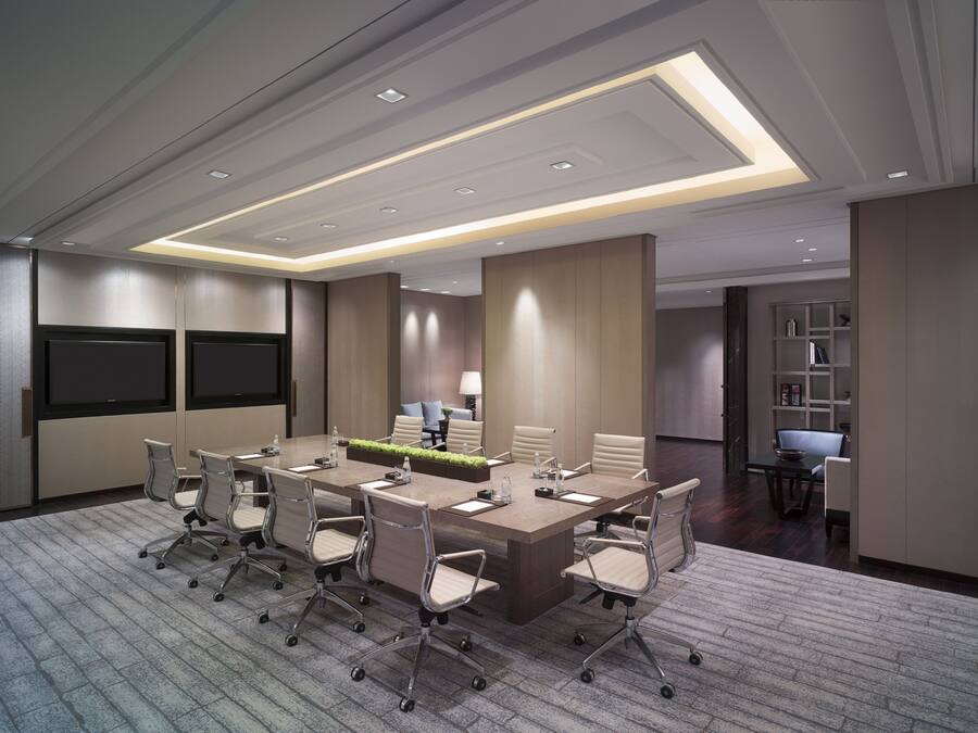 A modern conference room with a large rectangular table, multiple chairs, and built-in screens.