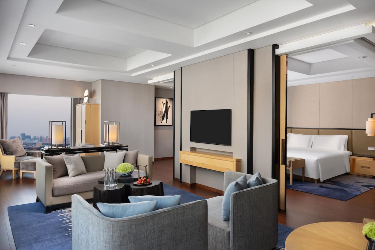 A modern hotel room with a sofa, a TV, a bed, and a desk.