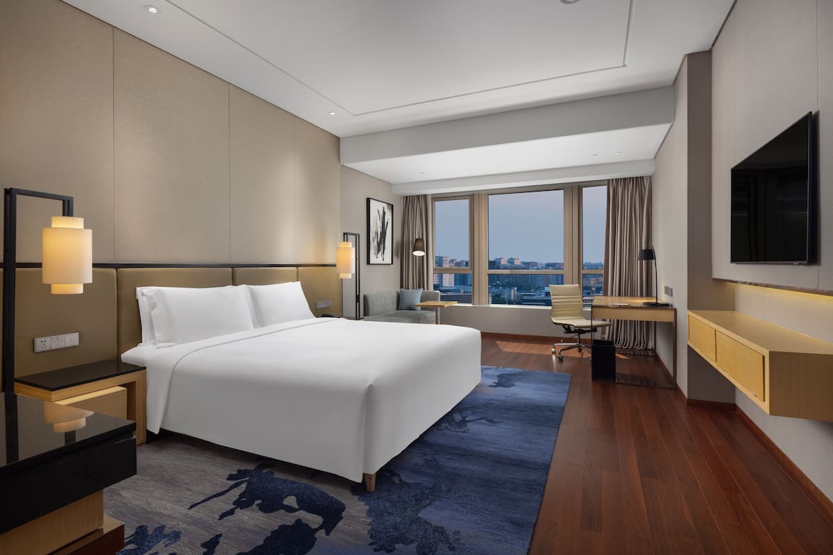 A modern hotel room with a large bed, a desk, and a view of the city.