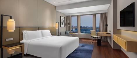 A modern hotel room with a large bed, a desk, and a view of the city.
