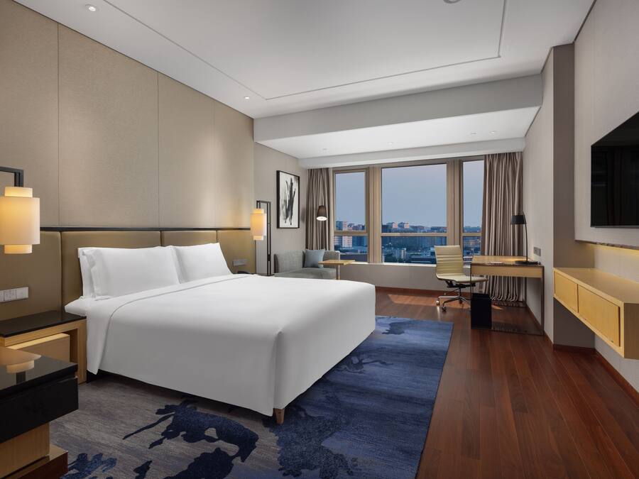 Quarto de hotel moderno com uma cama grande, uma escrivaninha e vista para a cidade.