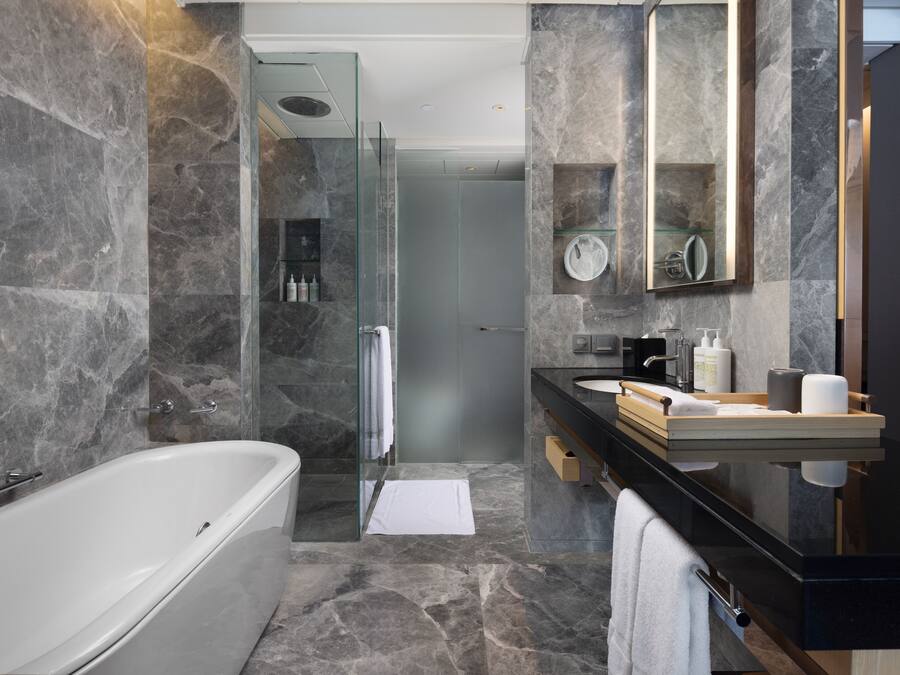 Un baño moderno con una bañera independiente, ducha con mampara de vidrio y tocador con encimera negra y salpicadero de mármol.