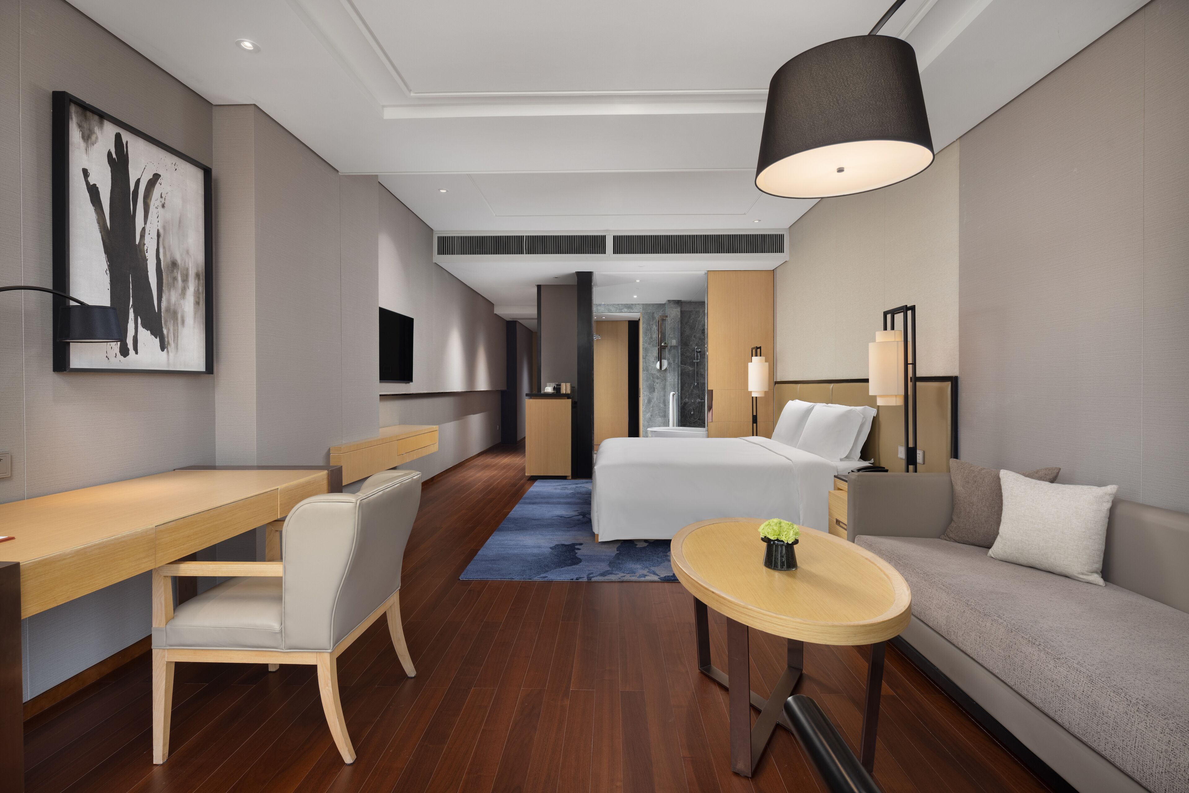 A modern hotel room with a wooden desk, a bed, a sofa, and a round table.