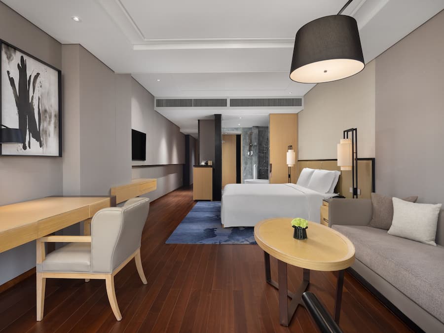 Een moderne hotelkamer met een houten bureau, een bed, een slaapbank en een ronde tafel.