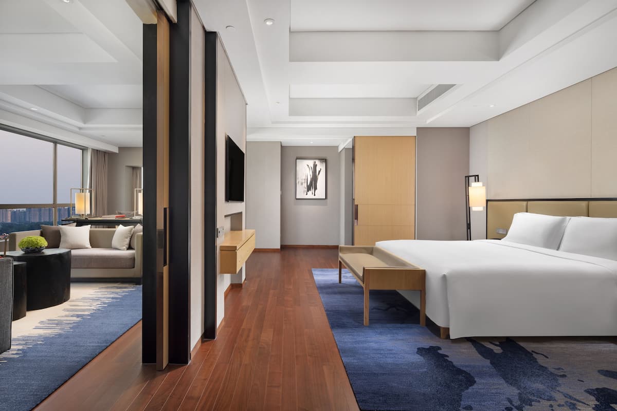 A modern hotel room with a large bed, a desk, a sofa, and a view of the city.