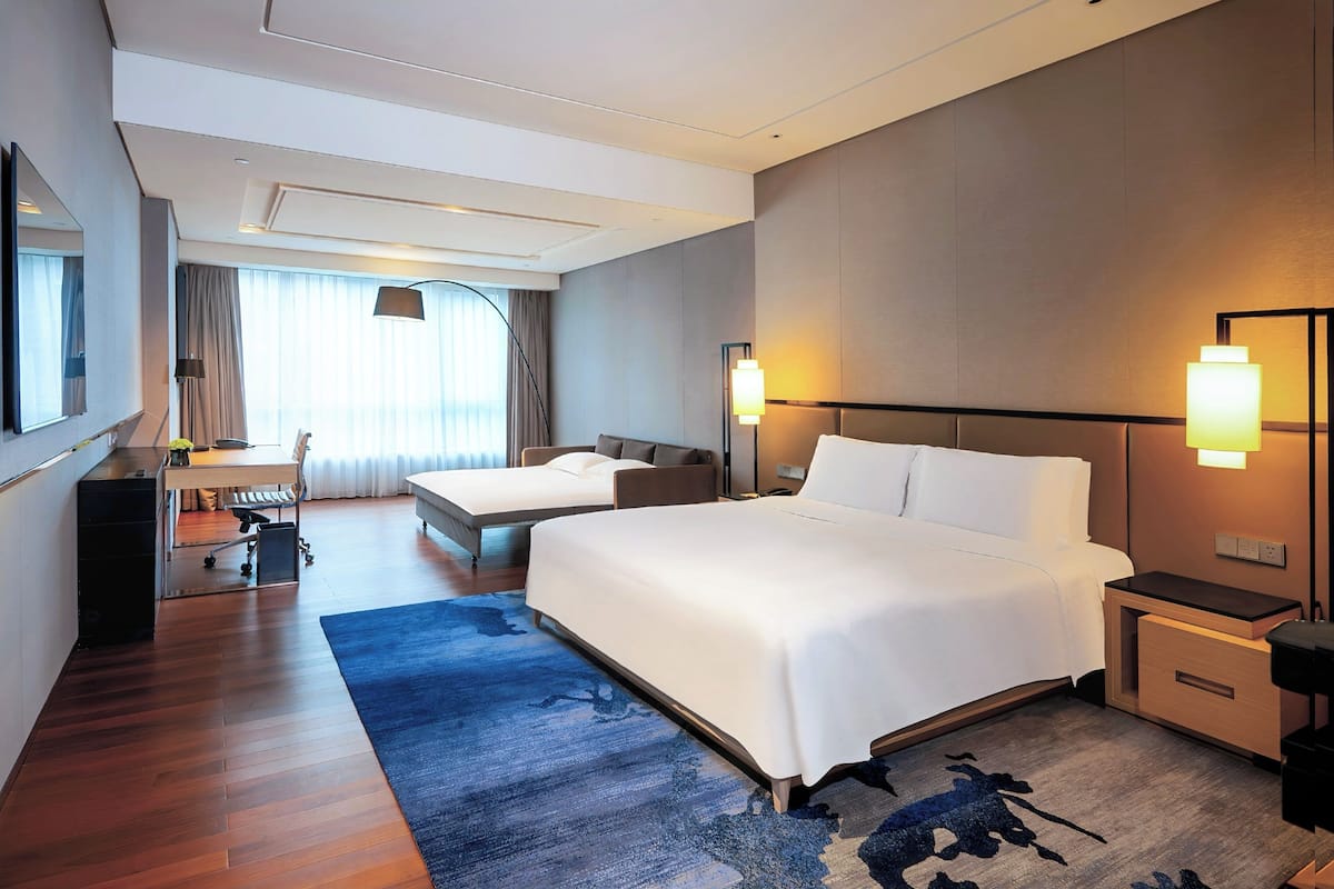 A hotel room with a large bed, a desk with a chair, a small sofa, and a desk lamp.
