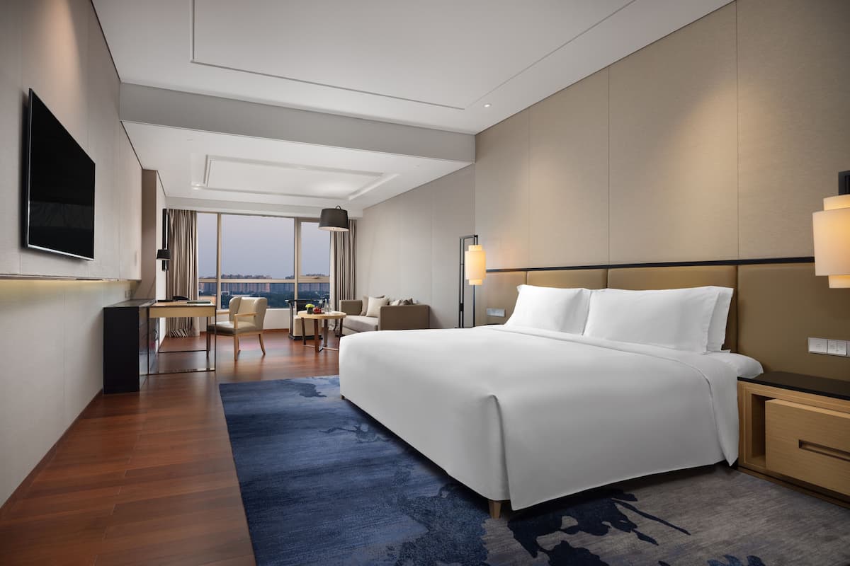 A modern hotel room with a large bed, a desk, a chair, and a view of the city.