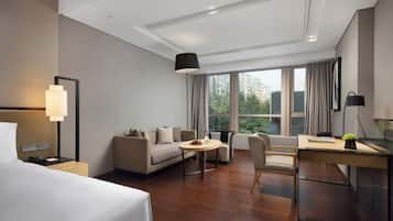 A modern hotel room with a bed, a sofa, a desk, and a dining table.