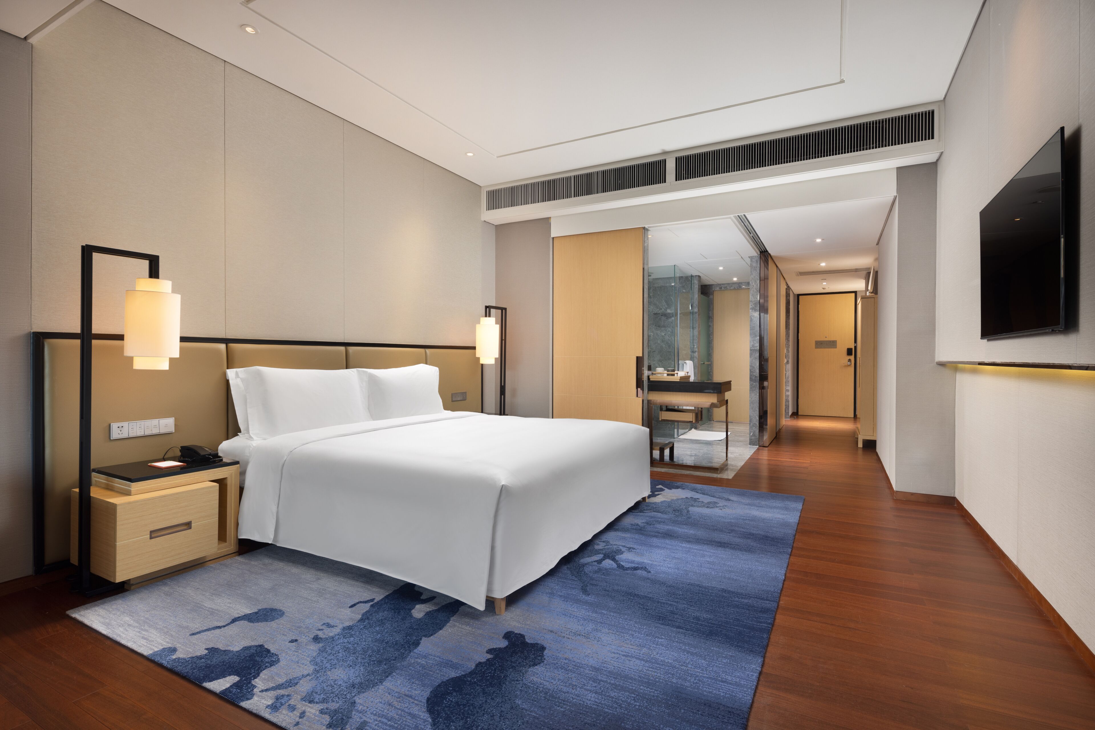 Habitación de hotel moderna con una cama grande, mesitas de noche, televisión y baño visible a través de una puerta abierta.