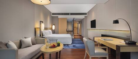 Una habitación de hotel moderna con sofá, cama, escritorio y mesa de comedor.
