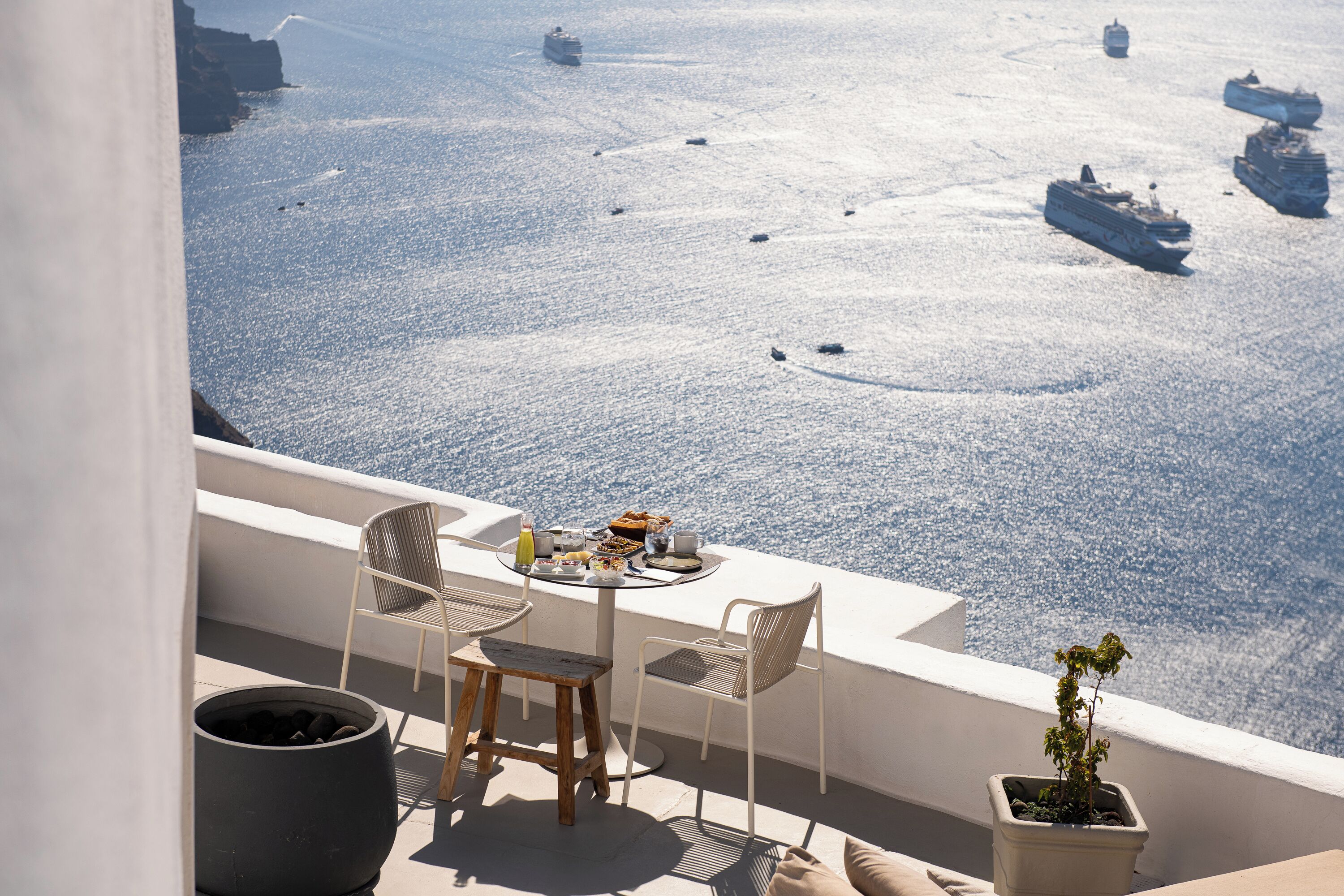 Ein Balkon mit einem Tisch für zwei Personen, Blick auf ein ruhiges Meer mit mehreren Schiffen.