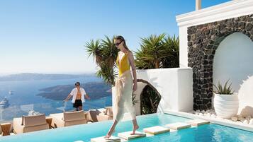 A pool area with a clear view of the sea, a stone wall, and a potted plant.