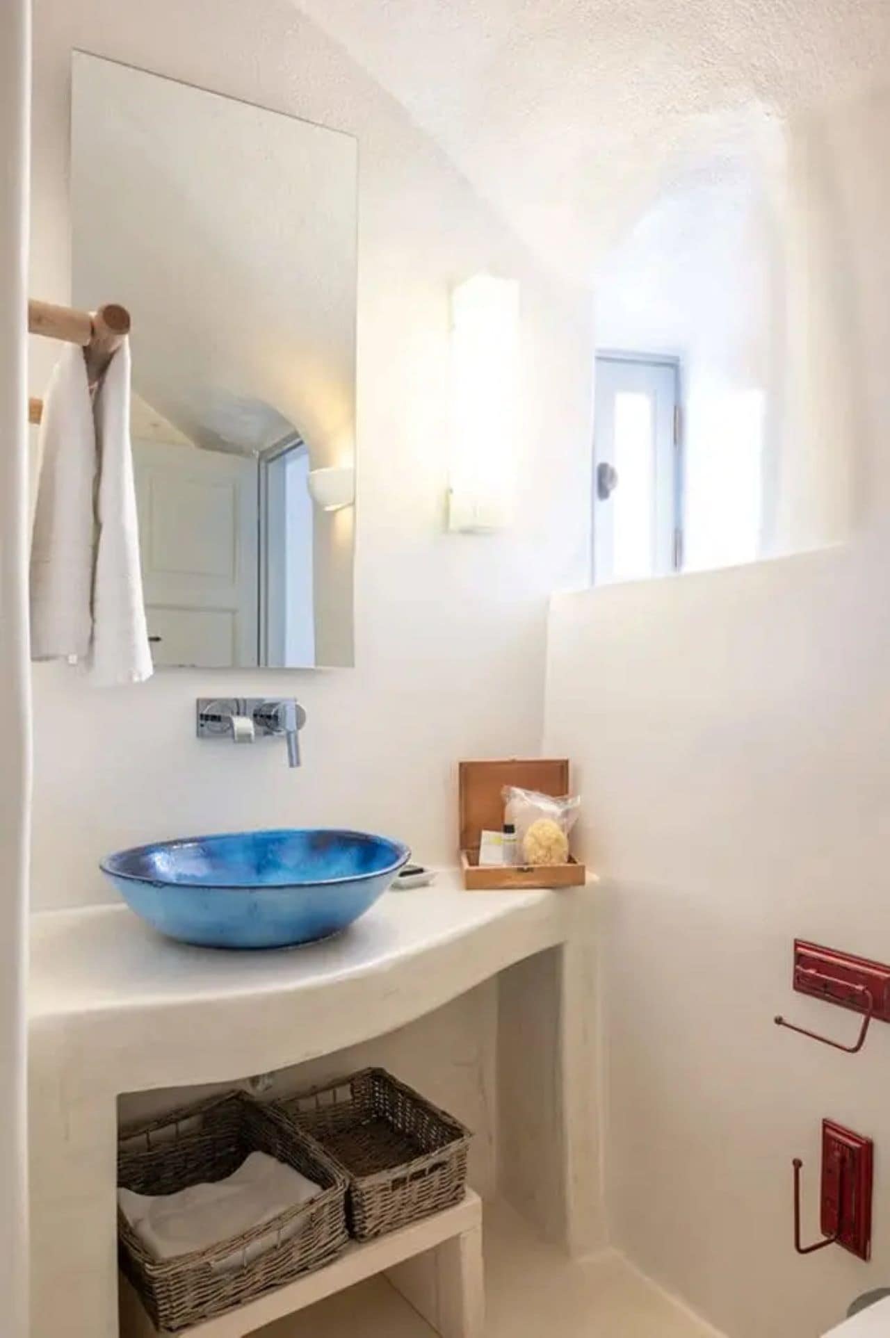 Une salle de bain avec un lavabo bleu, un miroir, un porte-serviettes, une petite boîte en bois et un panier.