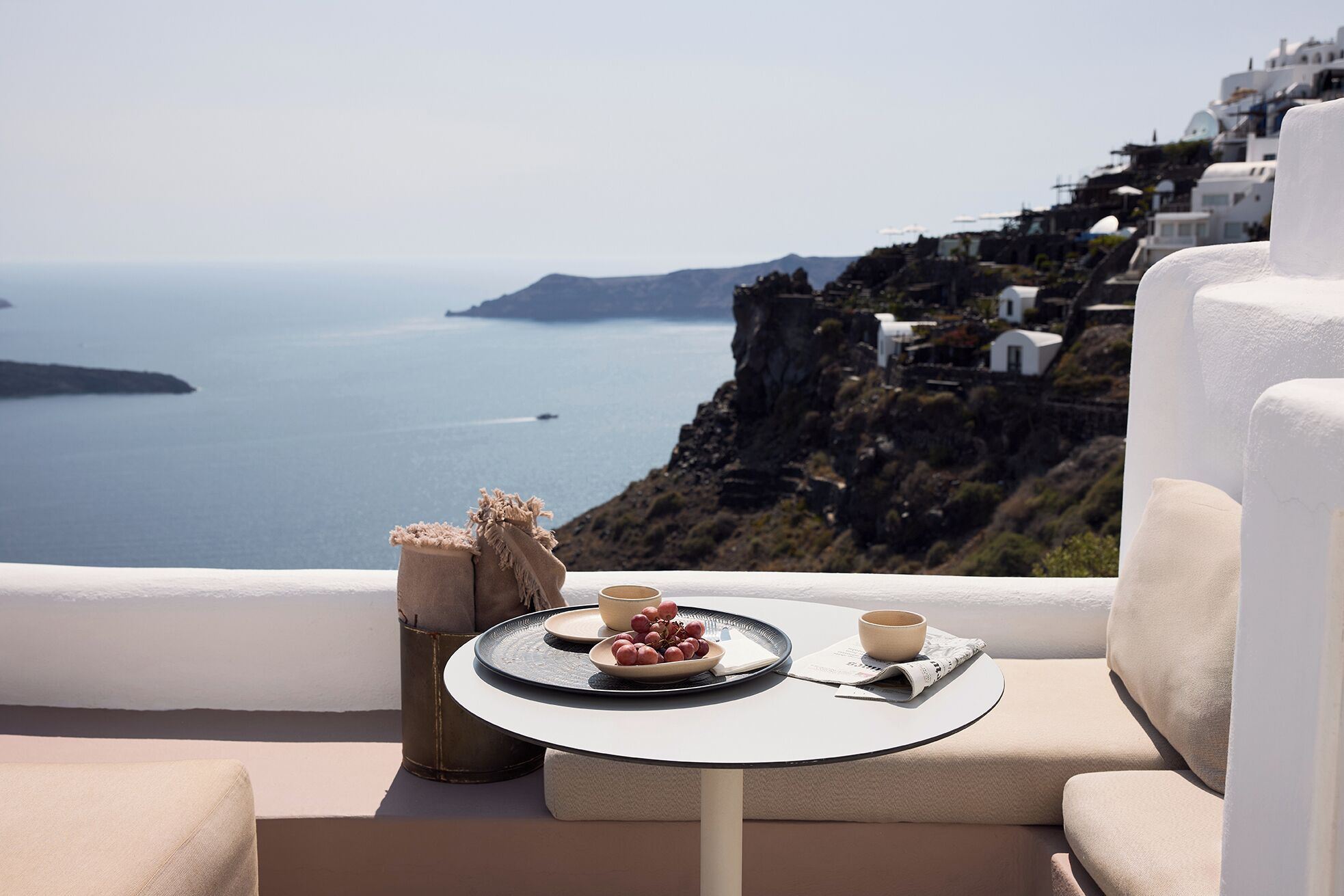 Un balcon avec une table dressée pour deux personnes, offrant une vue sur la côte, avec des bâtiments blancs et un ciel dégagé.