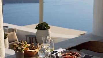 Una mesa lista para una comida, con platos, vasos y una planta en maceta, con vista a un cuerpo de agua.