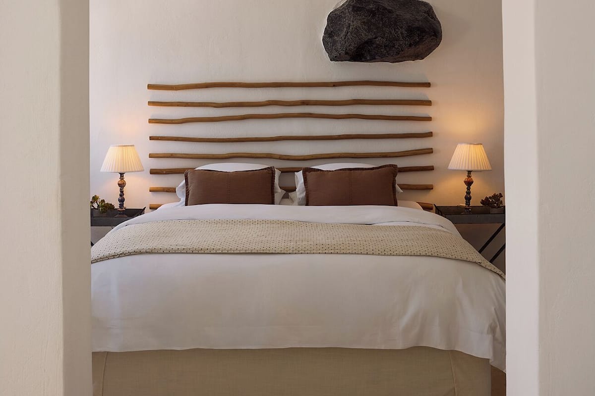 A bedroom with a bed, two bedside lamps, a rug, and a unique rock decoration on the wall.