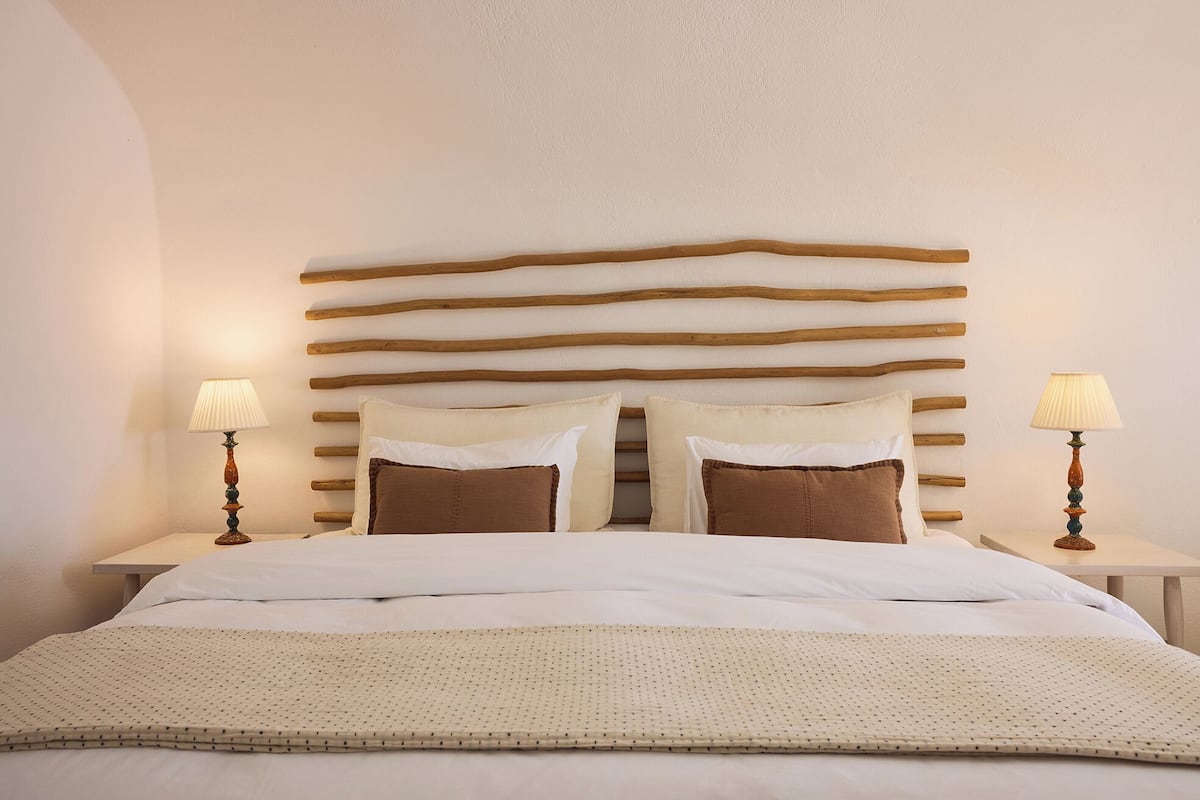 A neatly made bed with a headboard made of horizontal wooden slats, two bedside tables with lamps, and a beige quilt.