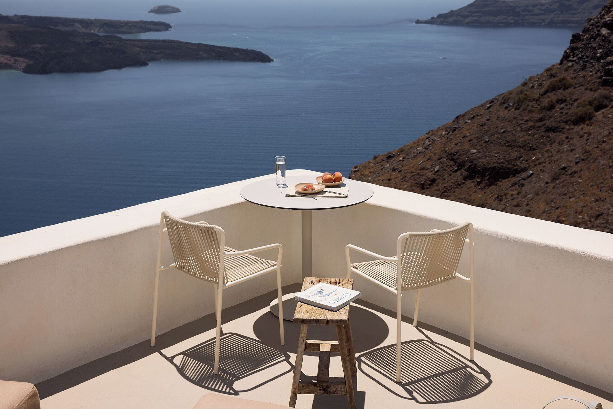 Un balcón con dos sillas blancas y una pequeña mesa redonda, con vistas al mar costero.