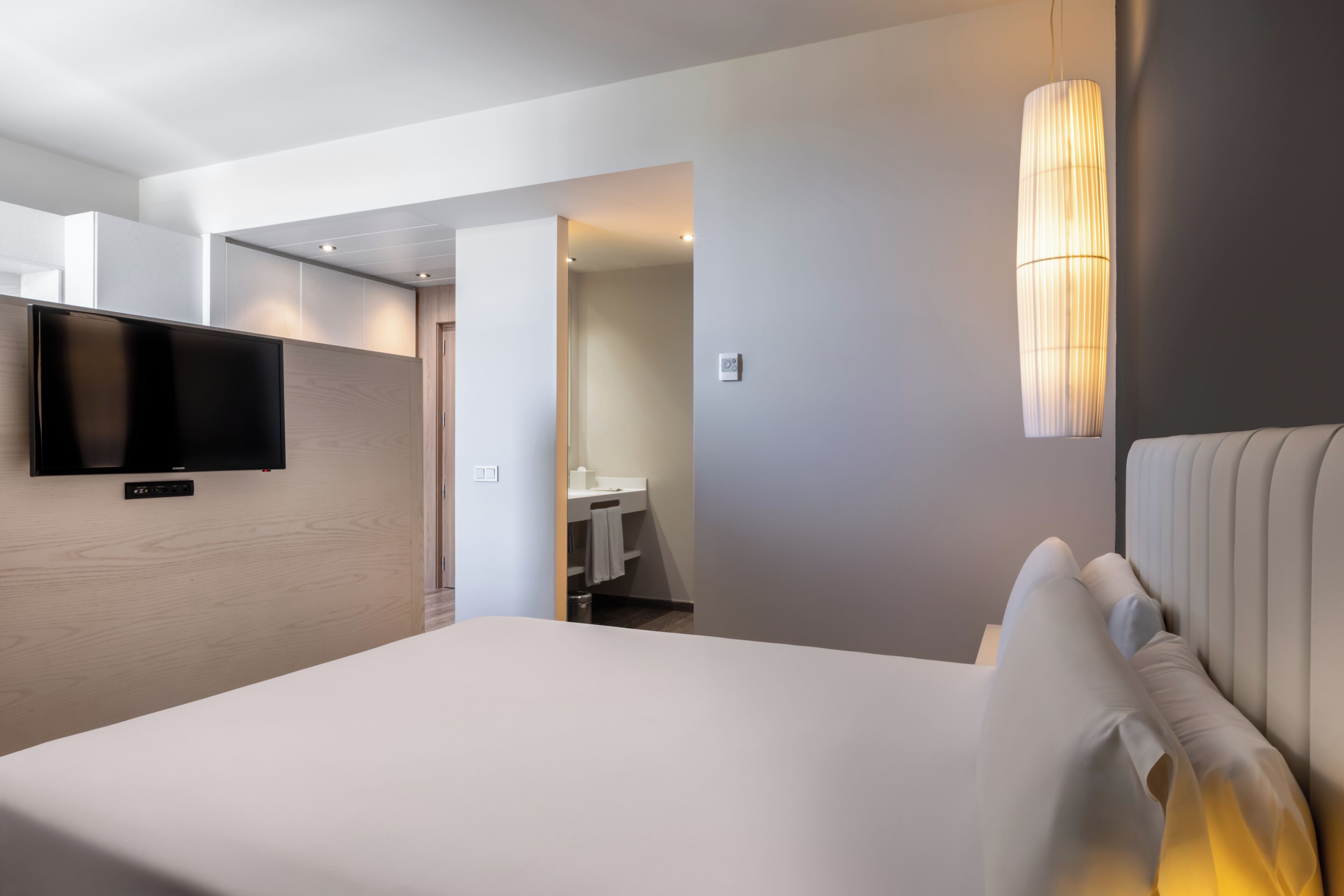 Et moderne hotelværelse med en seng, et fjernsyn ophængt på væggen og et badeværelse, der kan ses gennem en åben dør.