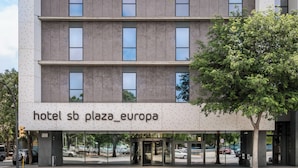 Un hôtel à la façade moderne, doté de grandes fenêtres et d’un arbre devant l’entrée.