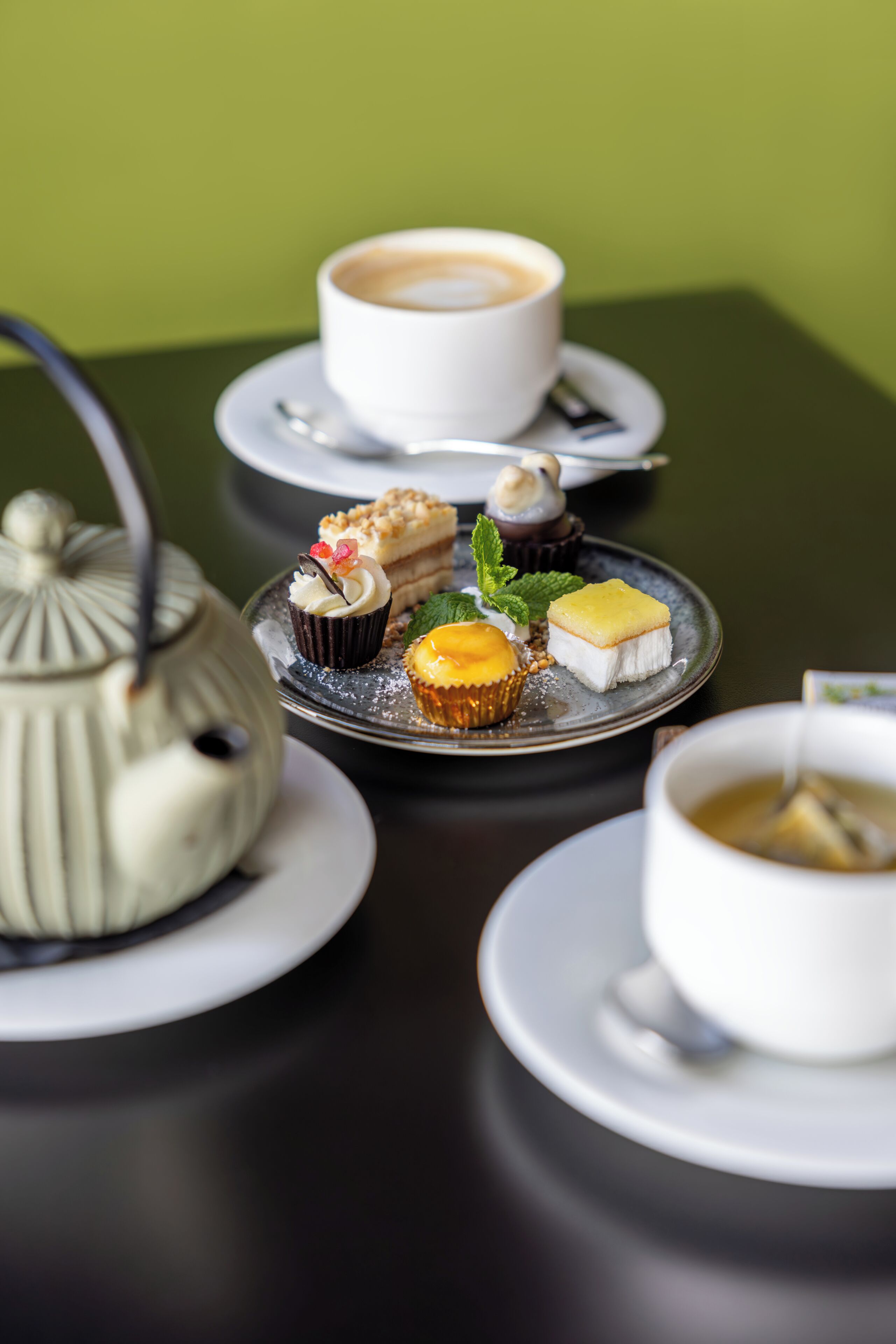 Une table avec une théière, une tasse de café et une assiette contenant diverses pâtisseries.