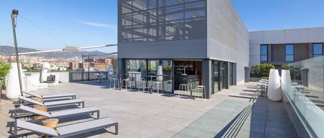 Una terraza en la azotea con mobiliario, un bar y vistas a la ciudad.