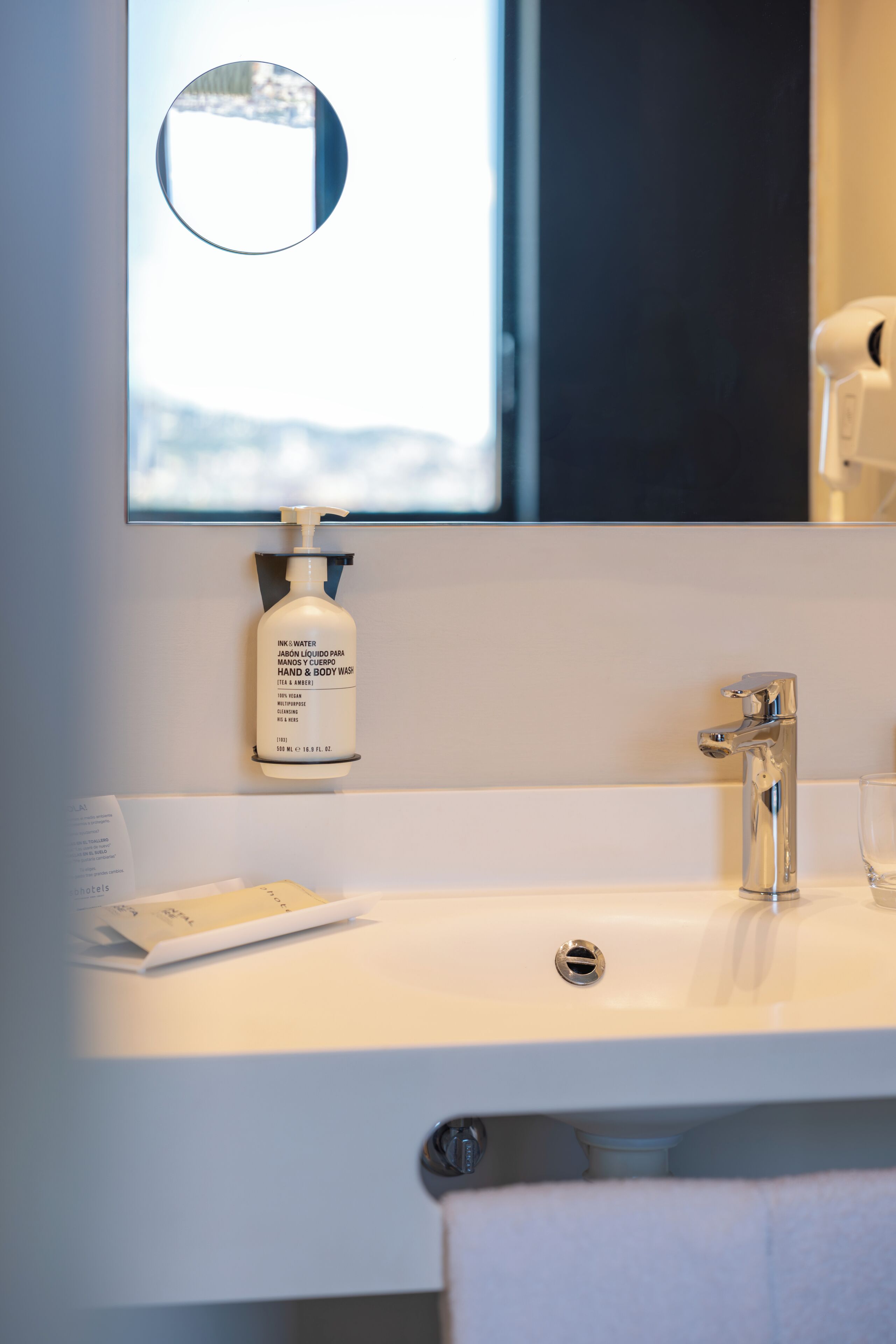 A bathroom with a white sink, a mirror, a bottle of hand soap, and a towel.