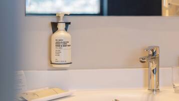 Een badkamer met een witte wasbak, een spiegel, een handzeepfles en een handdoek.