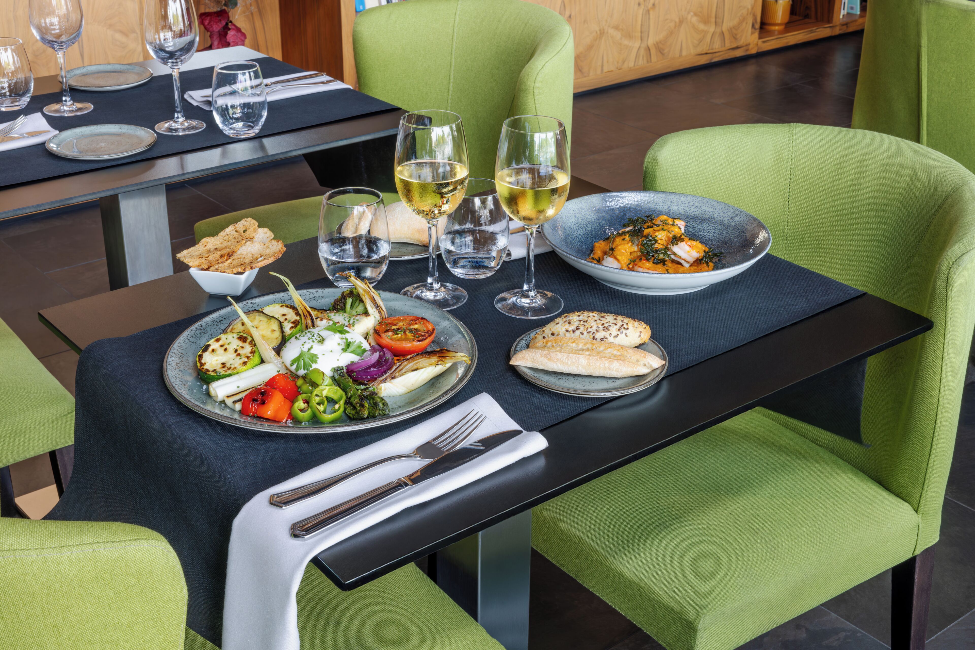 A dining table with plates of food, wine glasses, and cutlery.