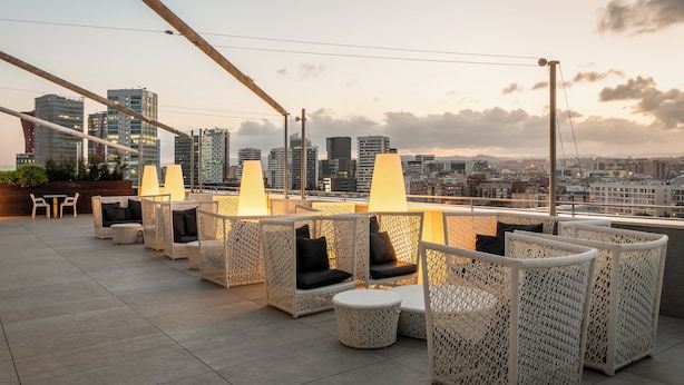 Une terrasse sur le toit, aménagée avec des meubles en osier, offrant une vue sur le panorama urbain et les bâtiments modernes.